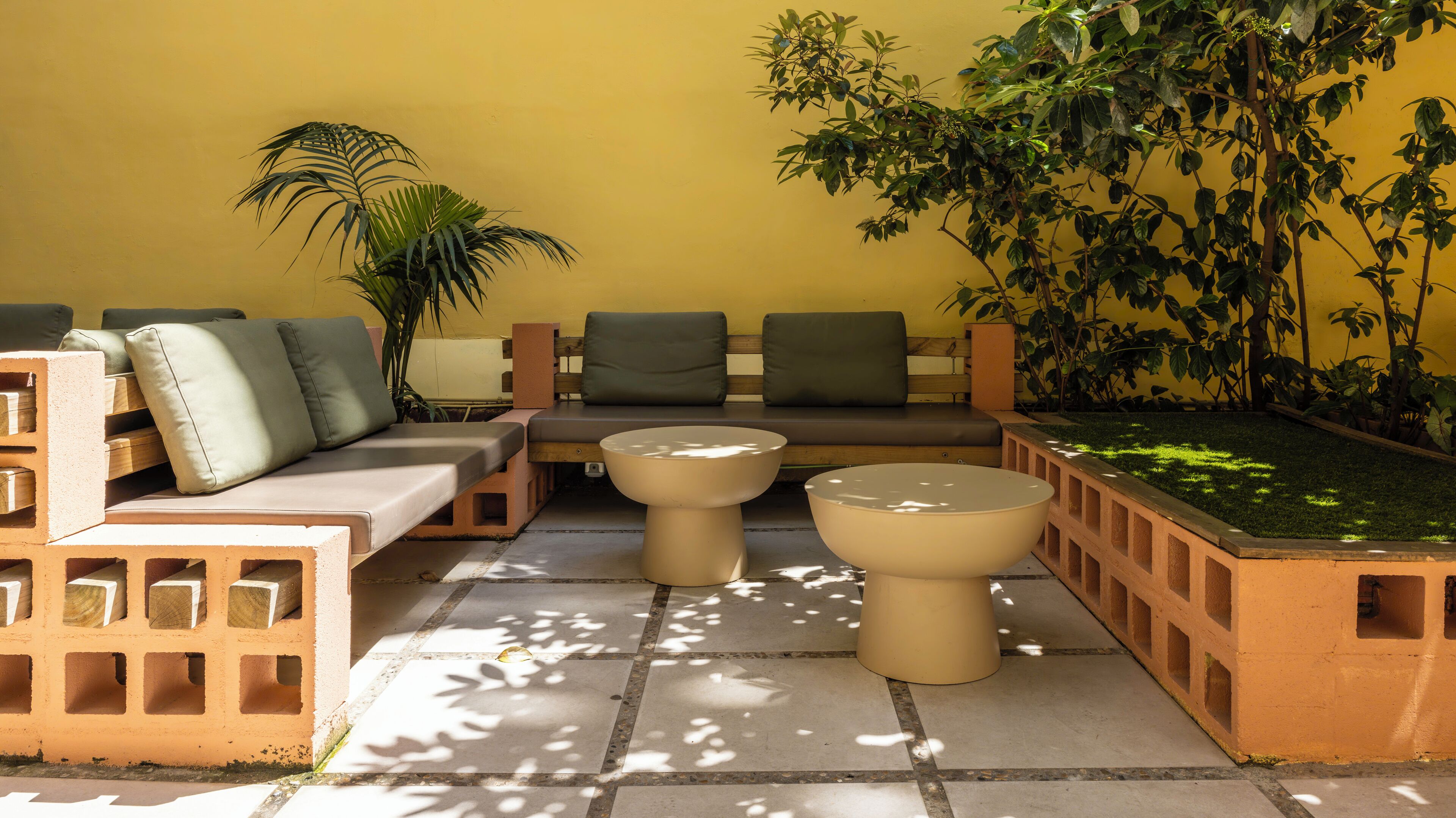A sunlit outdoor seating area with a sofa, two round tables, and potted plants.
