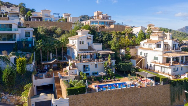 Un barrio residencial en una ladera, con varias casas, piscina y abundante vegetación.