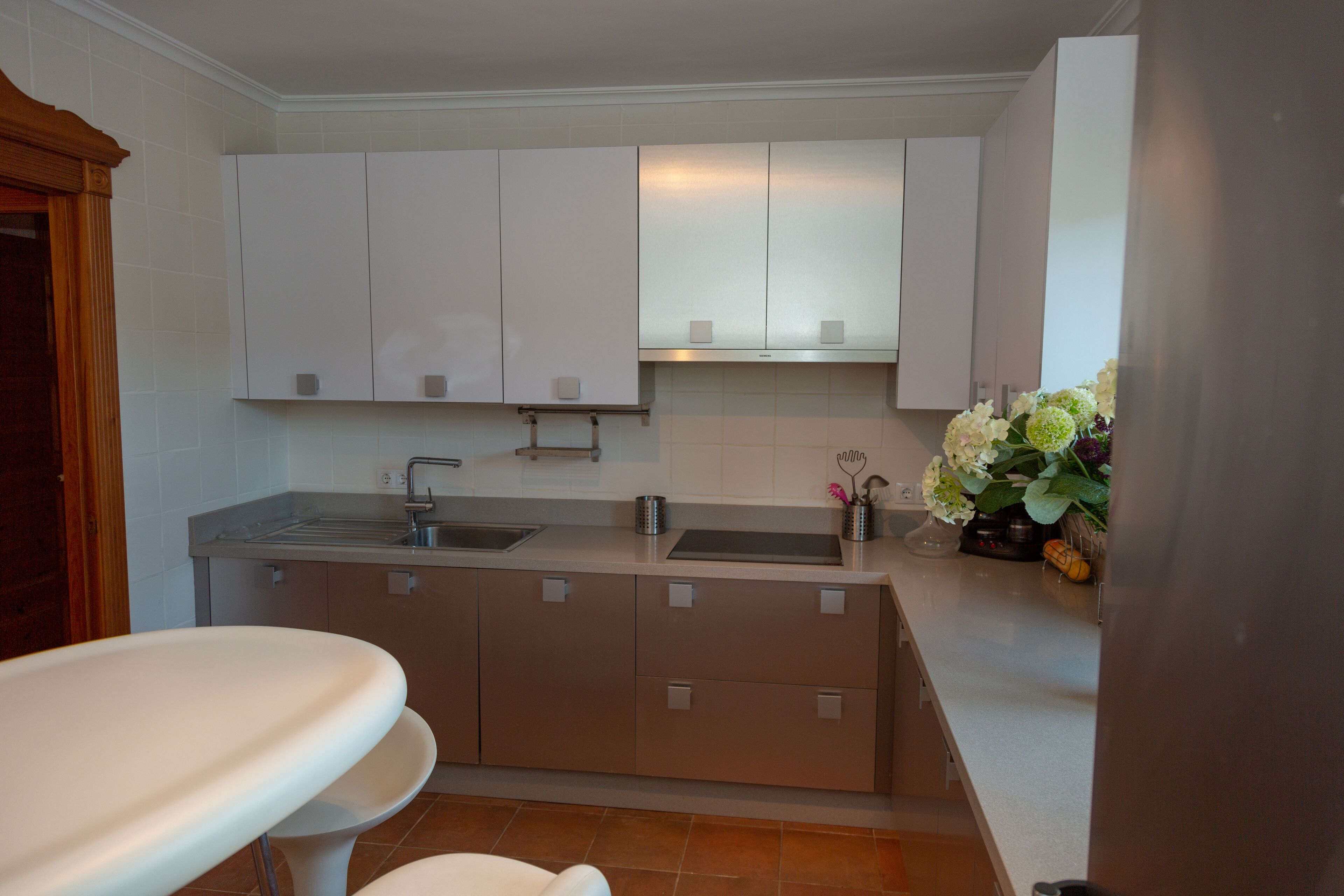Una cocina moderna con armarios blancos, un lavamanos y una encimera. Hay un florero con flores en la encimera.