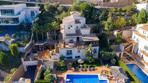 Una villa moderna con piscina, varios balcones y exuberante vegetación.