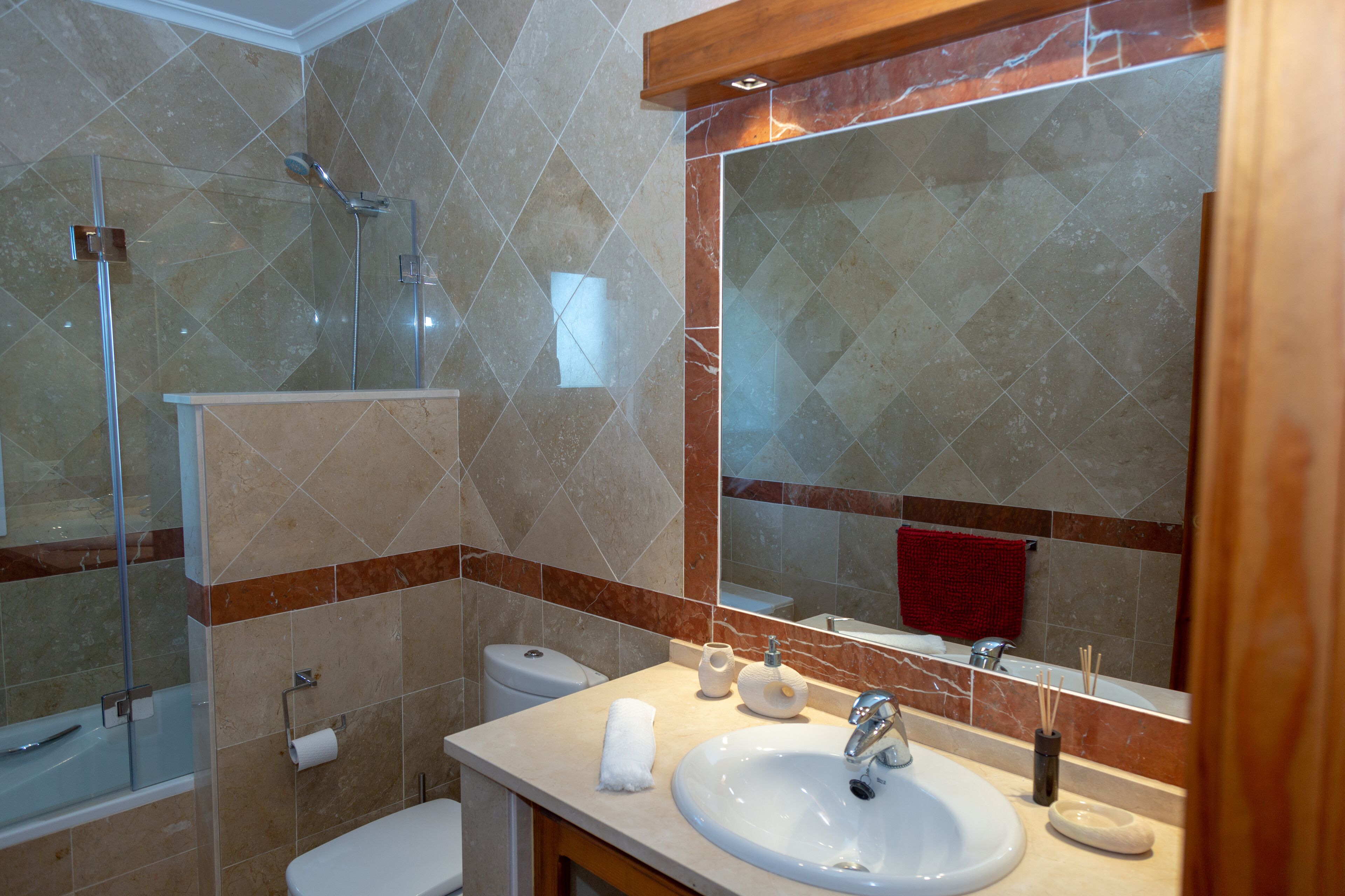 Un bany amb dutxa trencada per vidre, un lavabo blanc i un mirall gran.