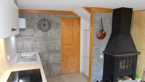 Eine Küche mit Steinrückwand, einer Holztür, einem schwarzen Herd und einem hängenden Topf.
