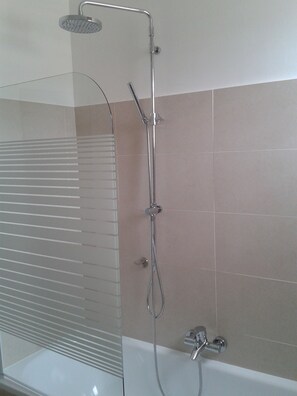 A modern bathroom with a glass shower enclosure, a handheld showerhead, a wall-mounted faucet, and a bathtub.