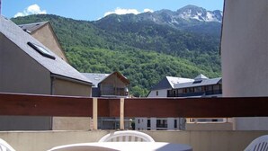 A balcony with white plastic chairs and a table, overlooking a mountain range and a village. - Nice triplex with balcony and mountain view, near ski- WIFI ACCESS (Saint-Lary-Soulan)