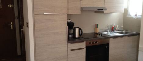 A compact kitchen with light wood cabinets, a stainless steel sink, and a built-in oven.