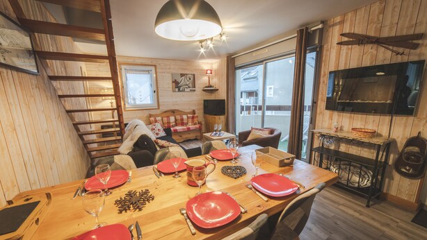 A cozy cabin interior with a dining table set for four, a television, and a wooden staircase. - Nice triplex with balcony and mountain view, near ski- WIFI ACCESS (Saint-Lary-Soulan)