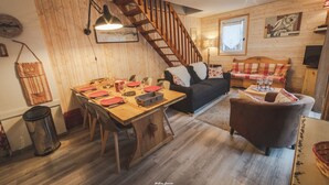 A cozy living room with a wooden staircase, a dining area with a table set for four, and a sofa. - Nice triplex with balcony and mountain view, near ski- WIFI ACCESS (Saint-Lary-Soulan)