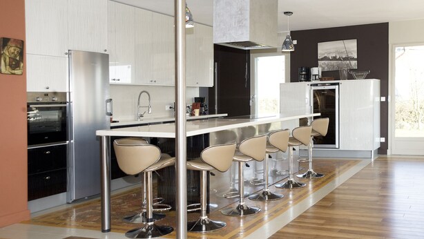 A modern kitchen with a central island, bar stools, stainless steel appliances, and a large window.