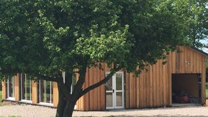 A wooden building with a garage door, a tree in front, and a gravel driveway.