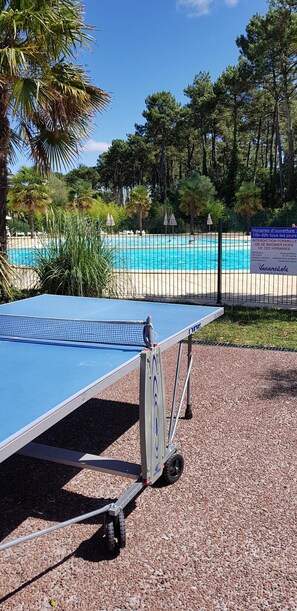 A portable ping pong table on a gravel surface with a pool and palm trees in the background. - Near the ocean tourist residence 3 * (Ondres)