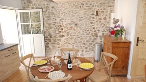 A stone wall kitchen with a wooden dining table set for two, featuring plates, glasses, and a bottle of wine. - Charming and comfortable loft-style gîte*** near Vichy for 4 to 5 people (Châteldon)