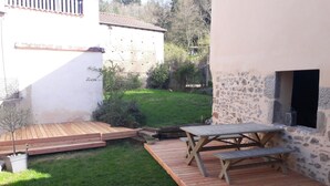 A patio area with a wooden table and benches, surrounded by a grassy lawn and a stone wall. - Charming and comfortable loft-style gîte*** near Vichy for 4 to 5 people (Châteldon)