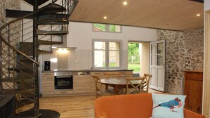 A modern kitchen with a central island, a dining area with a wooden table and chairs, and a spiral staircase leading to an upper level. - Charming and comfortable loft-style gîte*** near Vichy for 4 to 5 people (Châteldon)