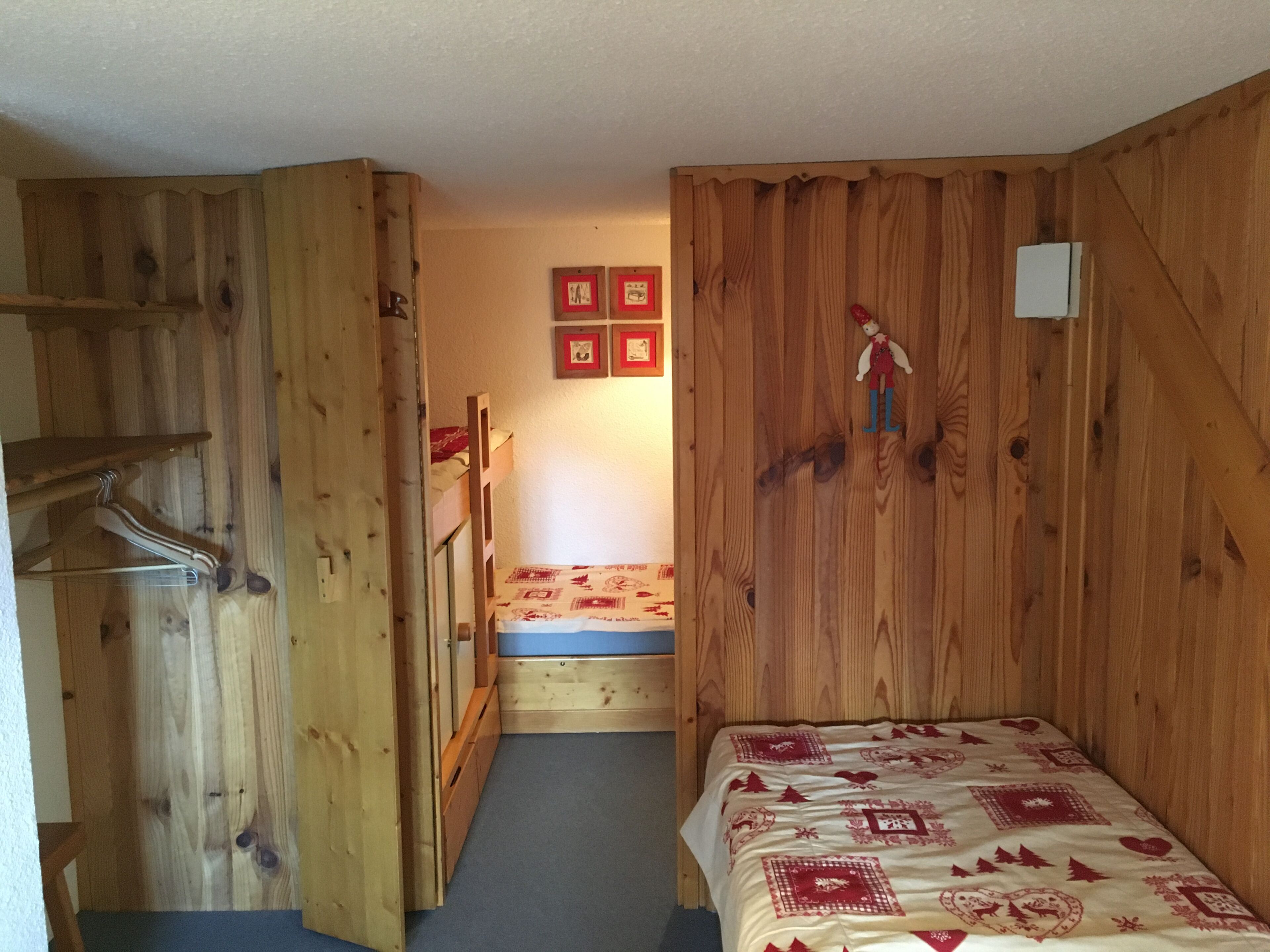 Una habitación pequeña de madera con una cama individual, un armario y una mesa pequeña.
