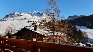 A wooden cabin with a snow-covered roof, surrounded by a mountainous landscape and a clear blue sky. - Chalet 12-14 people  Le Grand Bornand - Chinaillon  (Le Grand-Bornand)