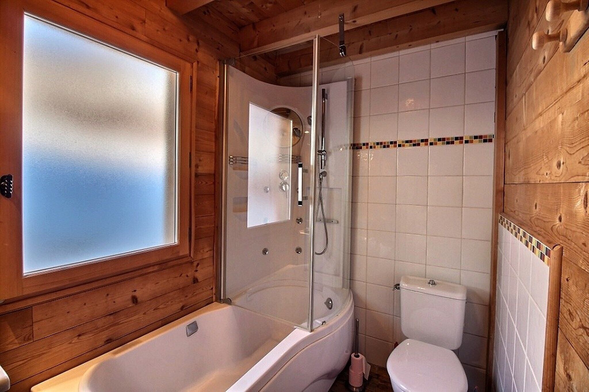 A wooden cabin bathroom with a glass-enclosed shower, a white bathtub, and a toilet.