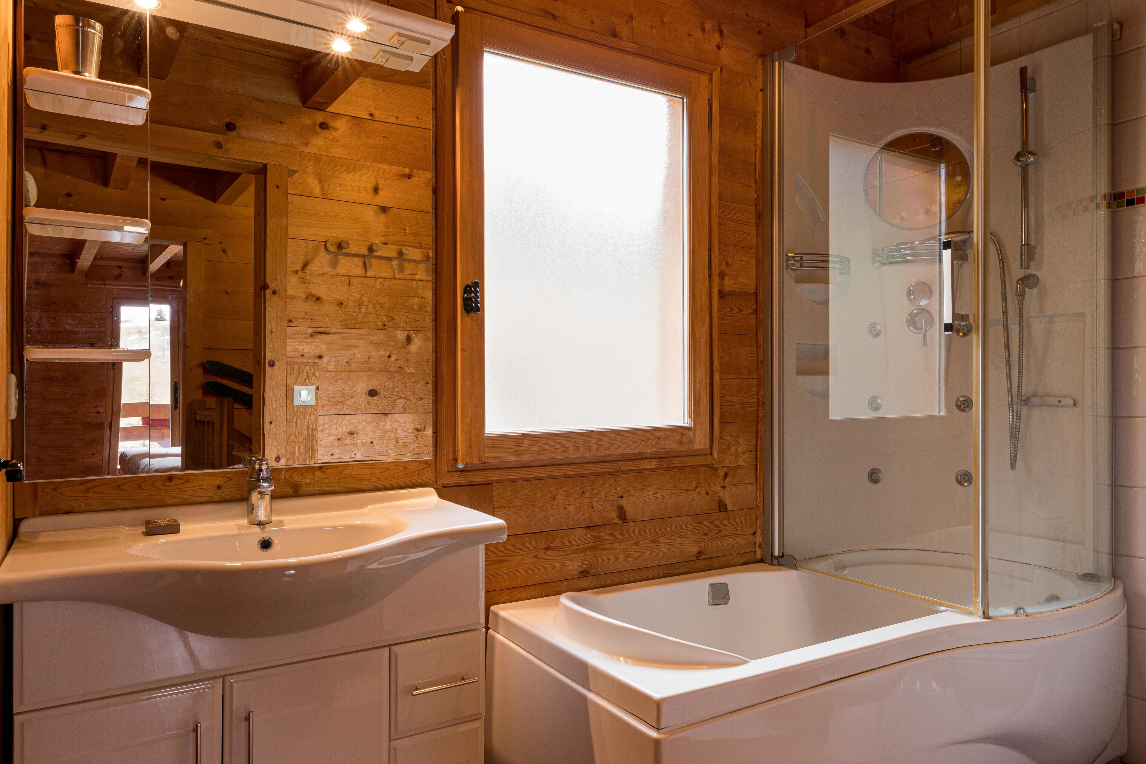 Une salle de bain rustique, aménagée dans une cabane en bois, avec un lavabo, un miroir et une douche à parois de verre.