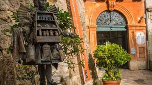 Une statue représentant une figure historique, vêtue d’un costume détaillé et agrémentée d’accessoires, est placée sur un piédestal devant un bâtiment dont l’entrée est richement décorée et qui arbore une bannière.