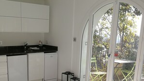 Un salon moderne avec un canapé blanc, une table basse en verre et une vue sur un jardin, visible à travers de grandes portes vitrées.
