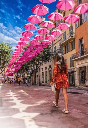 Calle flanqueada por edificios y sombrillas rosas.