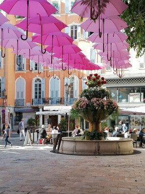 A public square with a central flower arrangement and multiple pink umbrellas overhead. - Apartment lux 1 bedroom, independent in villa, swimming pool, view Grasse and sea (Grasse)