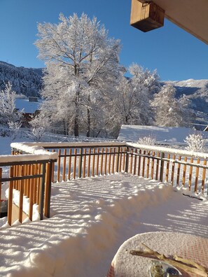A snow-covered deck with a wooden railing, a clear blue sky, and snow-covered trees in the background. - WEEKLY RENTALS, NIGHTS, summer-winter in GUILLESTRE (gateway to the Queyras) (Guillestre)