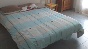 Un dormitorio con una cama, una silla de madera, un armario de madera y una lámpara roja con estampado de cuadros.