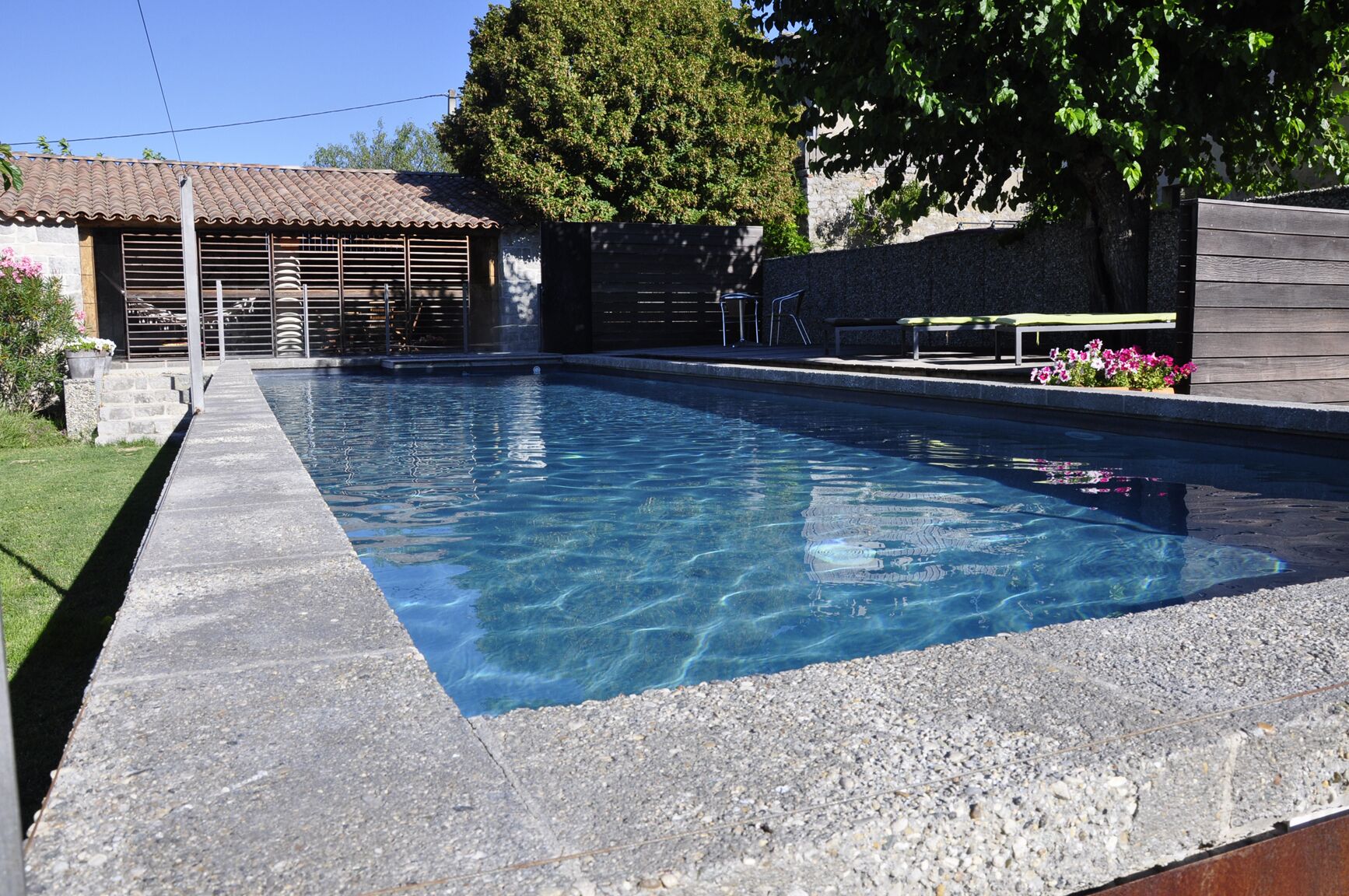 A rectangular swimming pool with clear blue water, surrounded by a stone deck.