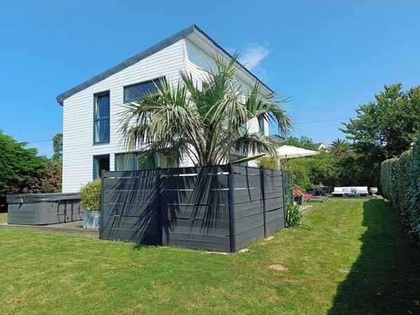 Een modern huis met twee verdiepingen, een zwart hek, een palmboom en een verzorgd gazon.