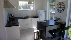 A modern kitchen with white cabinets, a black countertop, a stainless steel trash can, and a wall-mounted clock. - Bright house with garden and spa, 100 m from the beach. Pets welcome. (Plouguerneau)