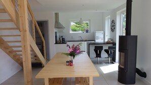 A modern kitchen with a wooden table, a black stove, and a view of the outdoors. - Bright house with garden and spa, 100 m from the beach. Pets welcome. (Plouguerneau)