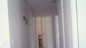 Un couloir étroit, dont le sol est recouvert de carreaux, mène à une pièce dotée d’une porte.