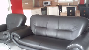 Un canapé en cuir noir dans un salon moderne, avec une cuisine en arrière-plan.
