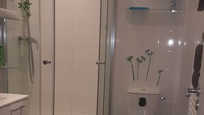A modern bathroom with a glass-enclosed shower, a toilet with a unique design, and a small shelf above the toilet. - Rental Apartment F3 Fontenay-aux-Roses (Fontenay-aux-Roses)