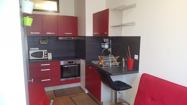 A compact kitchen with red cabinets, a microwave, an oven, and a black countertop. - Rental Apartment F3 Fontenay-aux-Roses (Fontenay-aux-Roses)