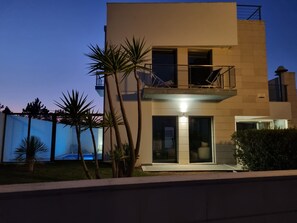 A modern two-story building with a balcony, large windows, and a well-maintained lawn.