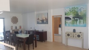 A modern dining area with a glass-top table, dark wooden chairs, and a dark wooden cabinet. There are two paintings on the walls, one depicting a cityscape and the other a landscape. - Villa d'ARCHITECTE, Sur les hauteurs, VUE MER, calme, TERRASSE 360°. (casal mota)