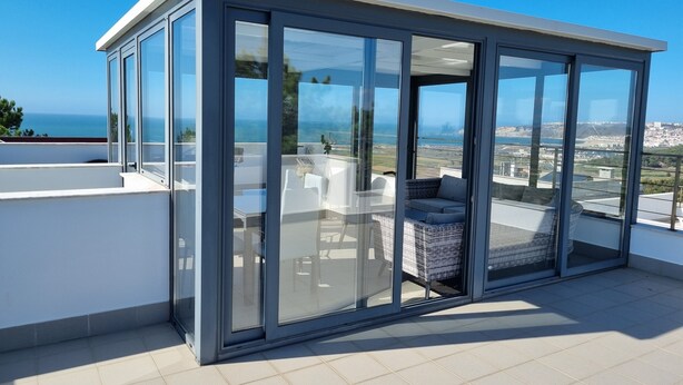 A modern glass-enclosed room with a view of the sea and cityscape. - Villa d'ARCHITECTE, Sur les hauteurs, VUE MER, calme, TERRASSE 360°.   (casal mota)