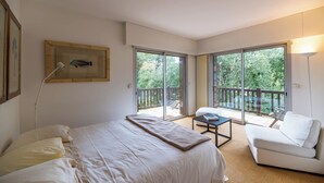 Un dormitorio con cama, sofá blanco, mesa y balcón con vista a zonas verdes.