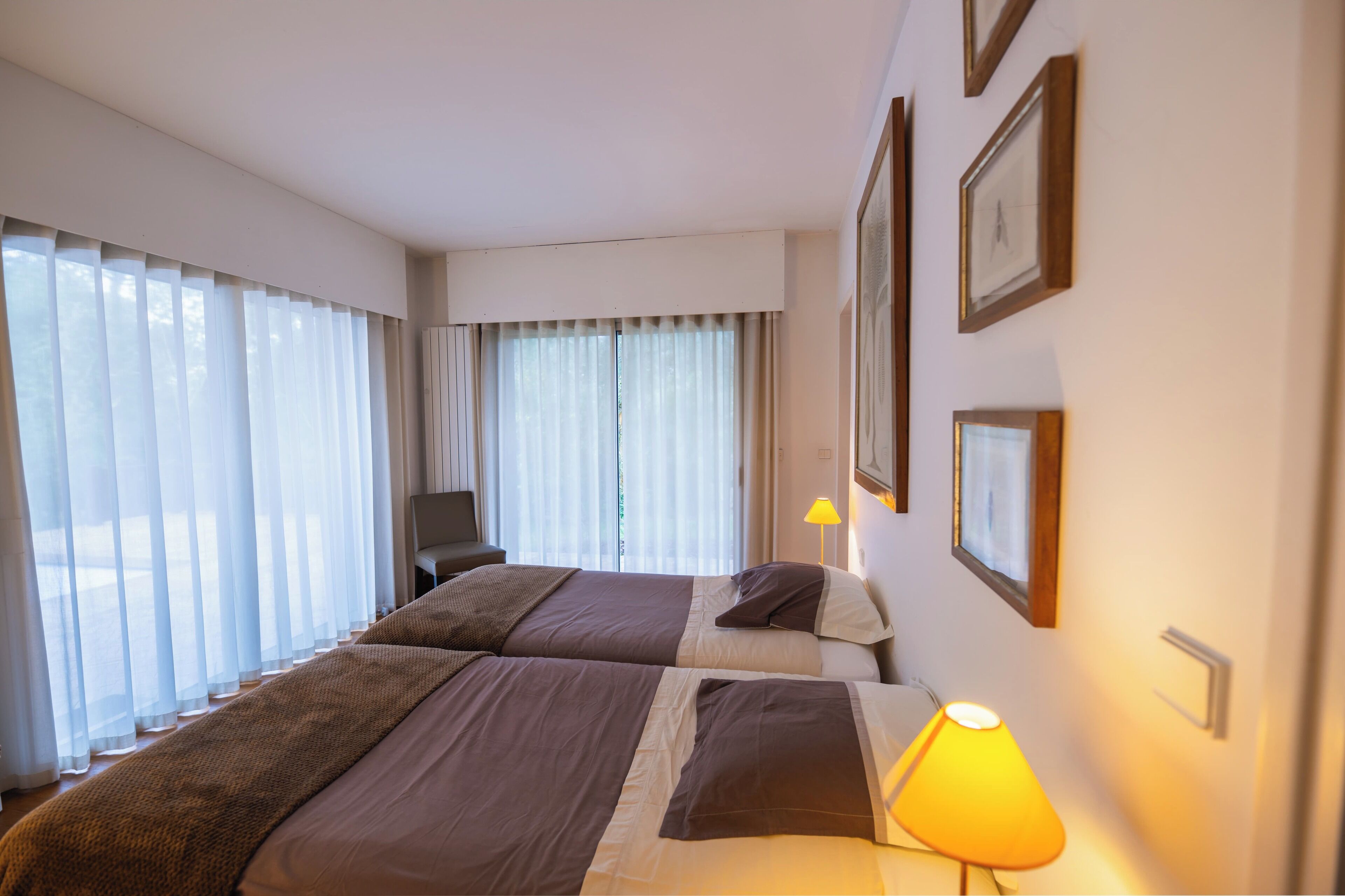 A hotel room with two beds, a desk, a chair, a lamp, and a window with curtains.