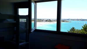 A room with a large window overlooking a beach and a clear sky.