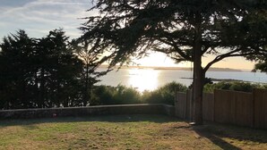 A backyard with a wooden fence, a swing, and a view of the sunset over a body of water.