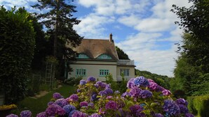 Una casa de techo pronunciado, rodeada de exuberante follaje y plantas en flor.