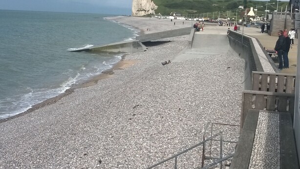 Una playa de guijarros con un muro de contención y escaleras que bajan hasta la orilla.