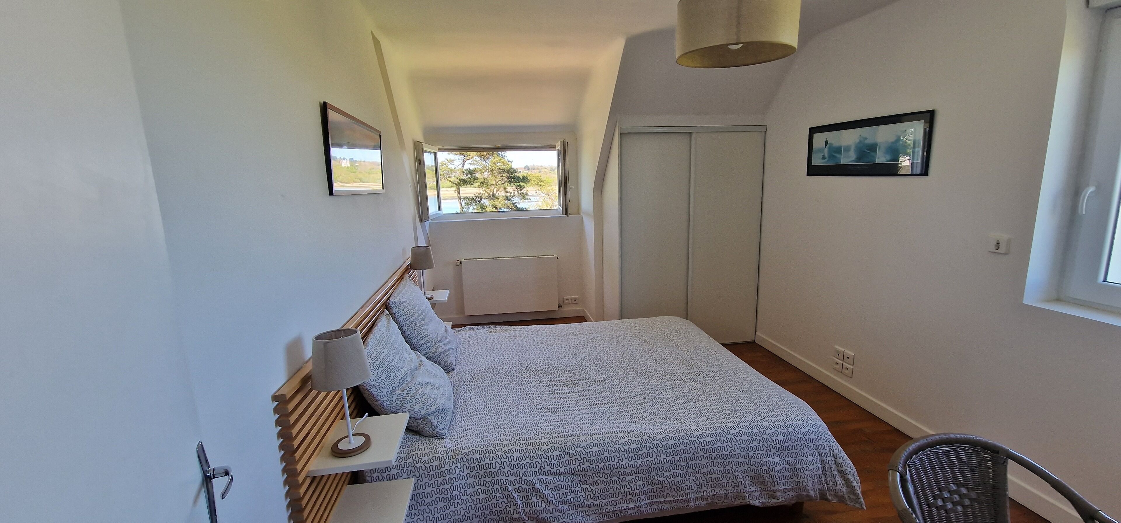 A bedroom with a bed, a chair, a radiator, a window, and a door.