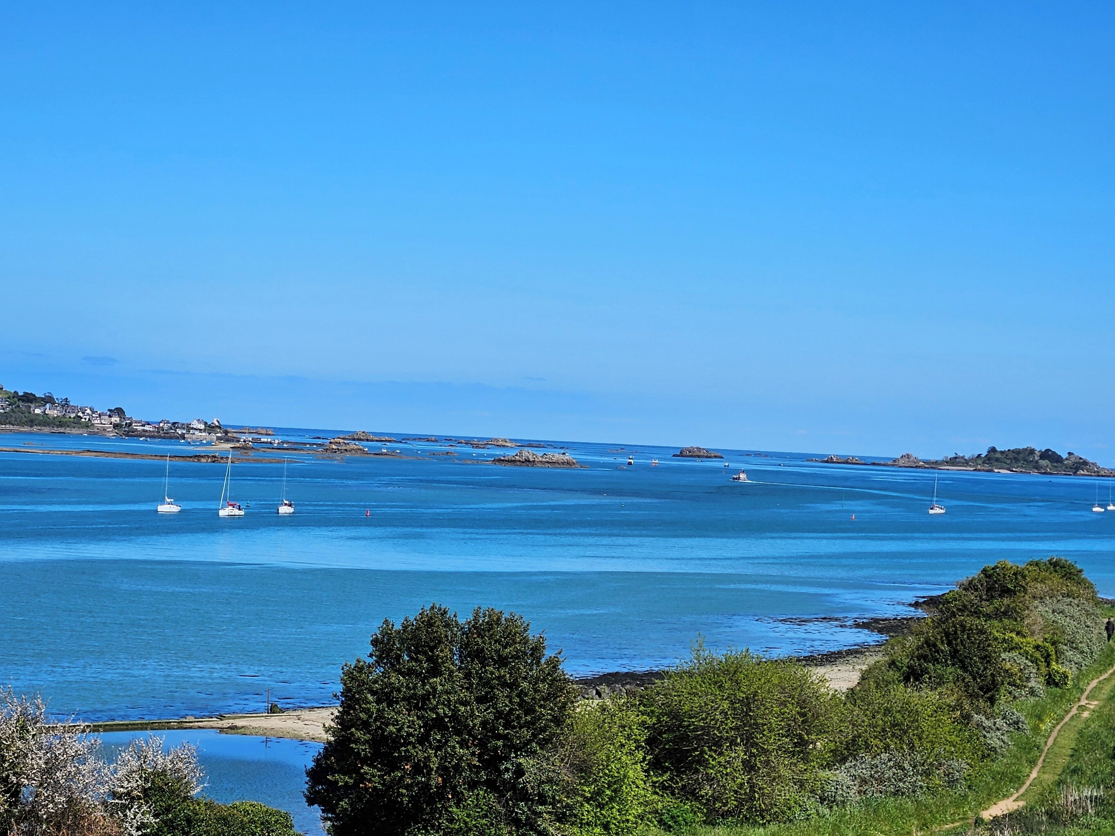 A coastal landscape with clear blue waters, boats, and a path leading to the beach.