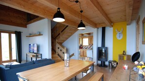 Un grand espace de vie comprenant une table à manger en bois, des bancs, un canapé et un téléviseur.