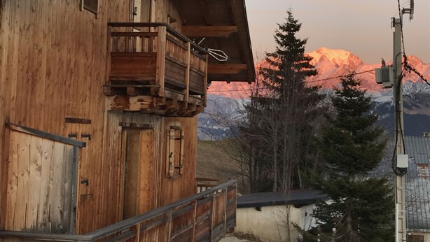 Un bâtiment en bois doté d’un balcon, avec une montagne en arrière-plan et une ligne électrique.