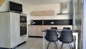 Eine moderne Küche mit Holzausstattung, einem eingebauten Backofen, einer Kaffeemaschine und einem Essbereich mit zwei Stühlen.