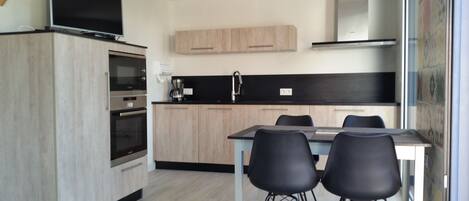 A modern kitchen with wooden cabinets, a built-in oven, a coffee maker, and a dining area with two chairs.
